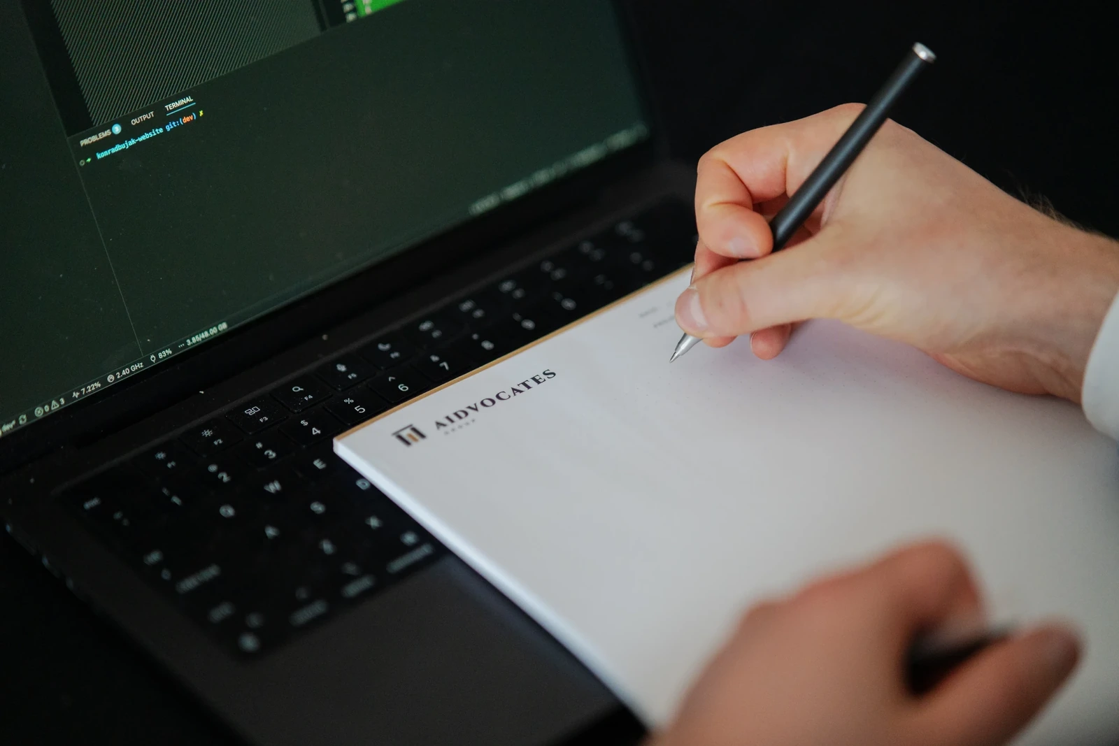 Dłoń podpisująca dokument obok otwartego laptopa